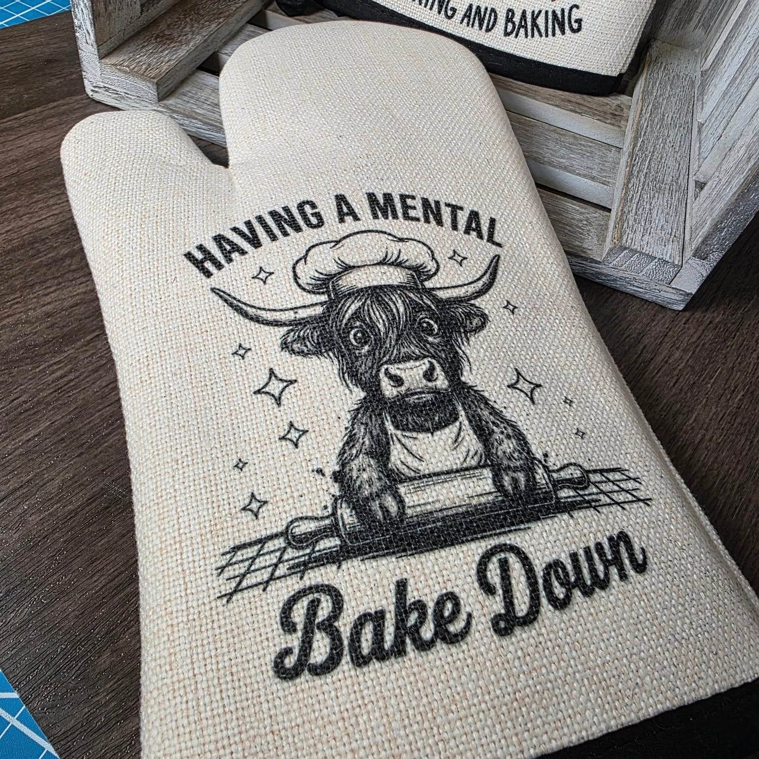 Oven mitt with cow illustration and text on a wooden surface