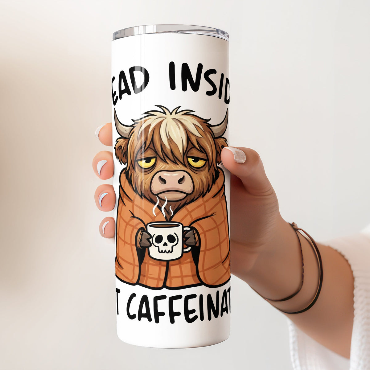Tumbler with a cartoon cow holding a coffee cup and text 'dead inside but caffeinated' held by a hand.
