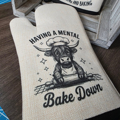 Oven mitt with cow illustration and text on a wooden surface